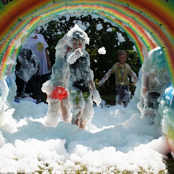 Children covered in foam playing under a rainbow arch.