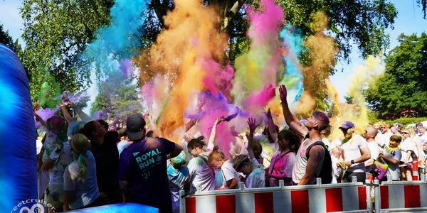 Crowd celebrating with colorful powder at an outdoor event.
