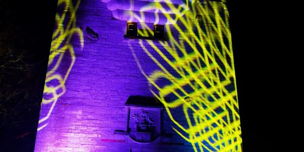 Historic tower illuminated with purple and yellow light patterns at night.