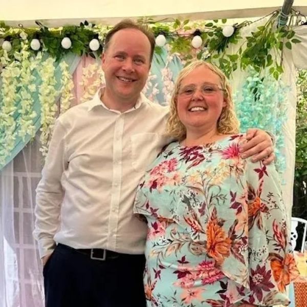 A happy couple posing in front of floral decorations at an event.