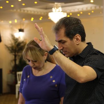 Man raising hand with eyes closed, woman looking down in a softly lit room.