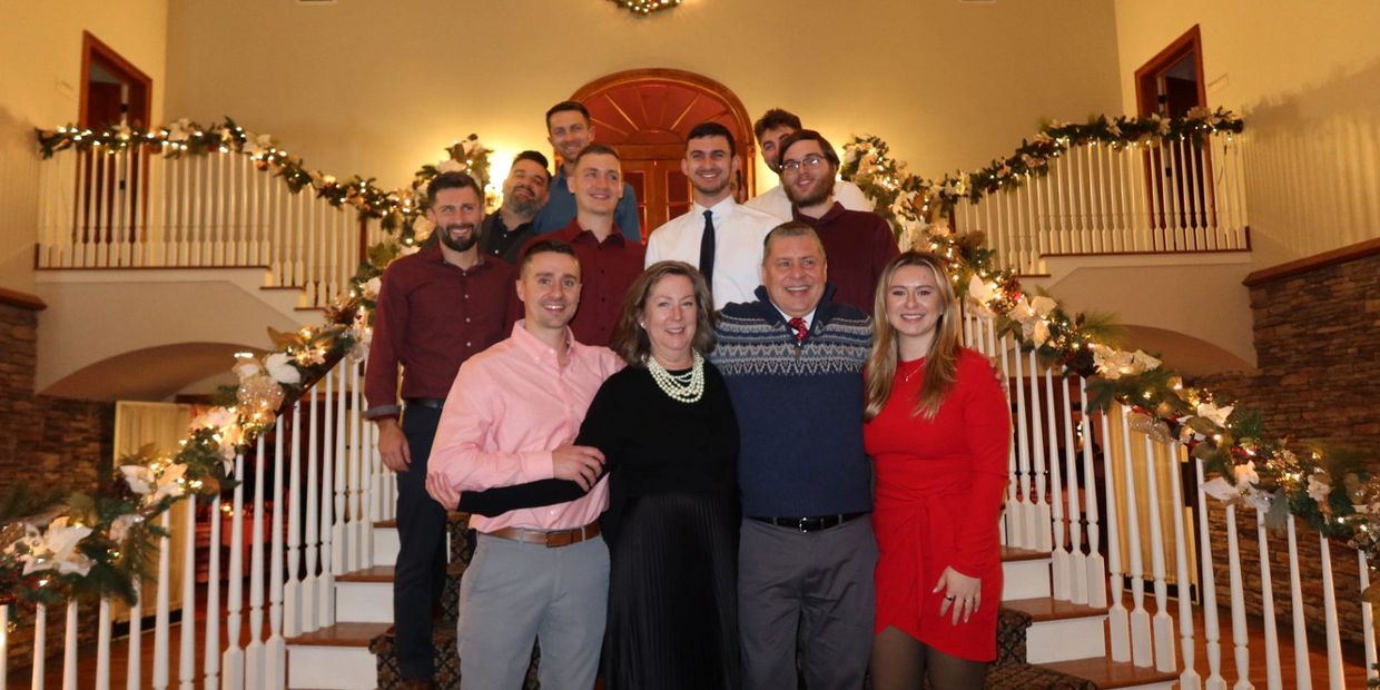 Family gathered on staircase decorated with Christmas lights and wreath.