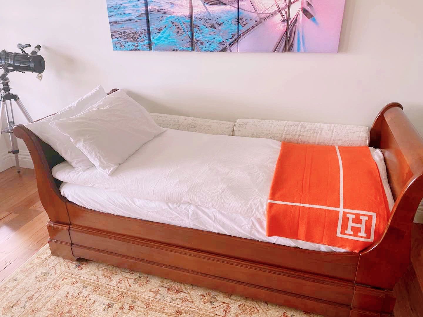 Wooden daybed with white bedding and an orange blanket.