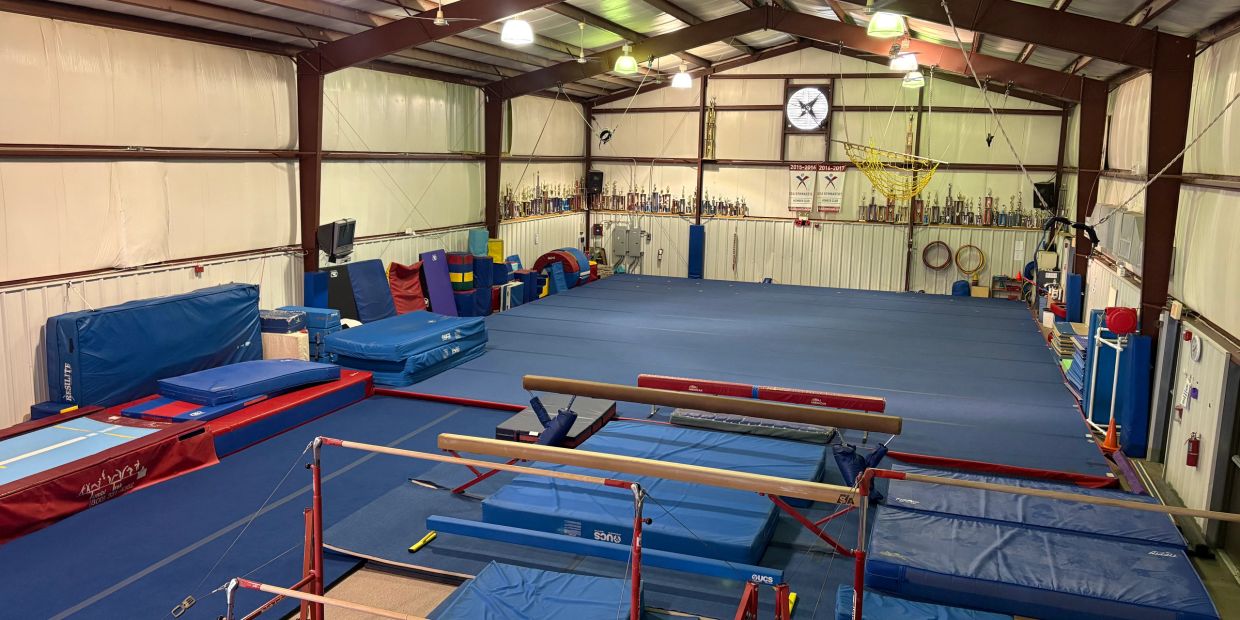Indoor gymnastics gym with equipment and mats.