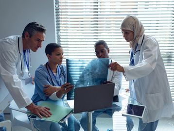4 physicians seriously looking at a large computer screen