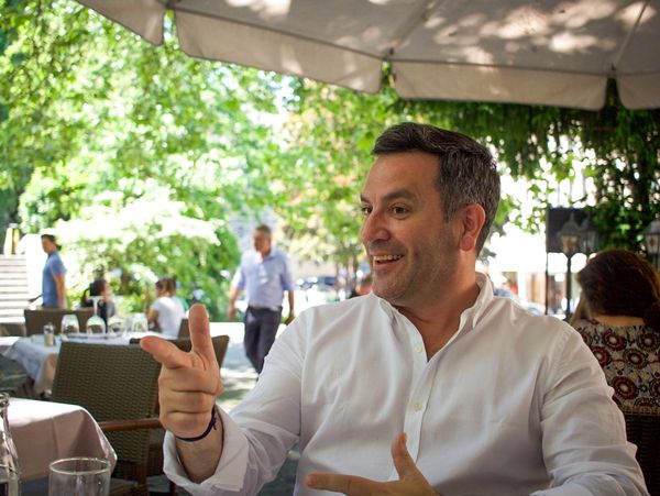 Man in white shirt gesturing and smiling at an outdoor café.