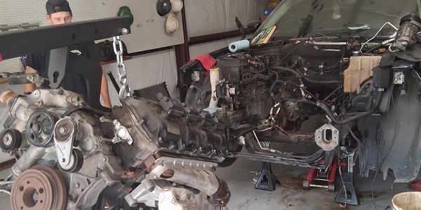 A man removes a car engine using a hoist in a garage.