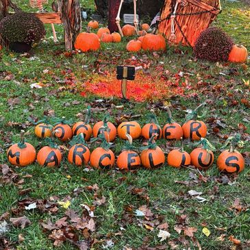 Mini pumpkins spell out "TOGETHER MAROONOUS" on grass with fall leaves.