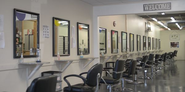 Empty hair salon with multiple styling stations and chairs lined up.