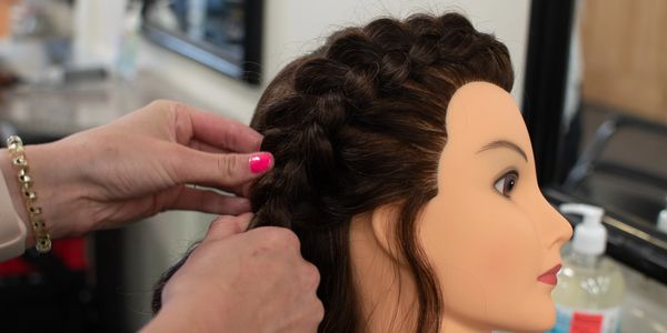 Hands braiding hair on a mannequin head in a salon setting.