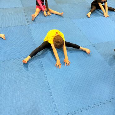 Children stretching their legs on a blue mat in a group exercise.