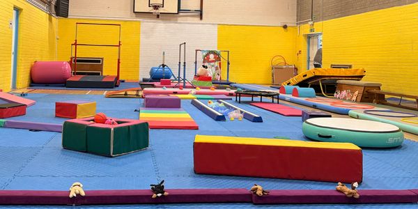 Colorful gymnastics equipment set up in a gymnasium with blue mats and yellow walls.