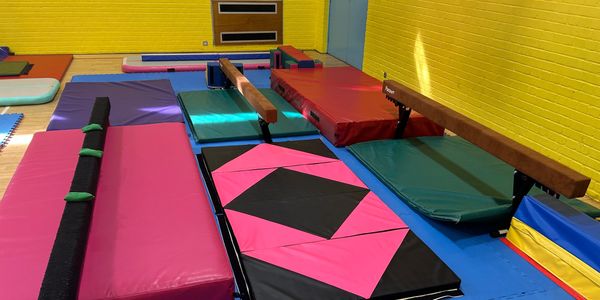 Colorful gymnastics mats and balance beams in a bright gym.