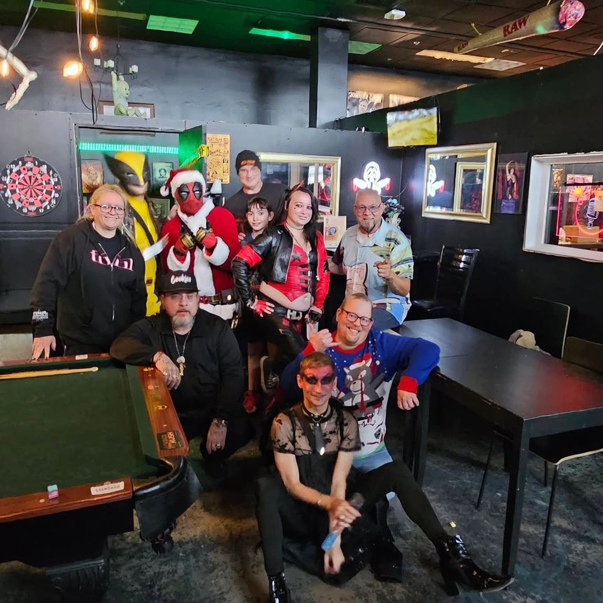 Group of friends in costumes posing in a game room with a pool table and dartboard.