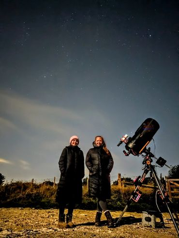Two happy women and a telescope after a stargazing experience near Brighton