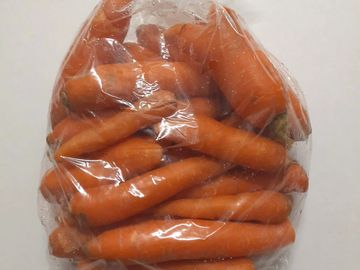 A clear plastic bag filled with fresh orange carrots.