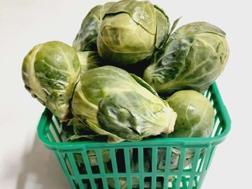 Fresh Brussels sprouts in a green plastic basket on a white surface.