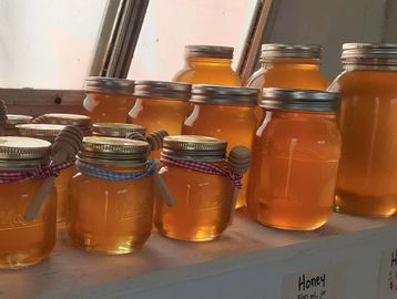 Rows of jars filled with golden honey, some adorned with ribbons and wooden honey dippers.