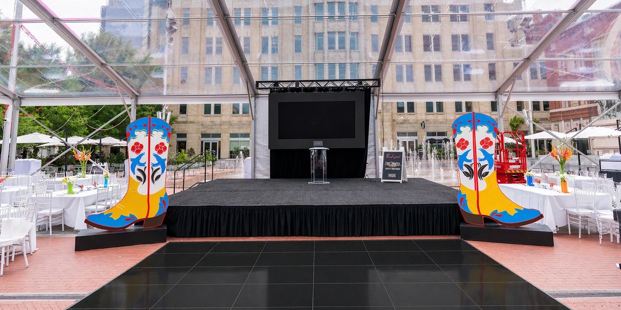 Outdoor event stage with colorful cowboy boot decorations under a clear tent.