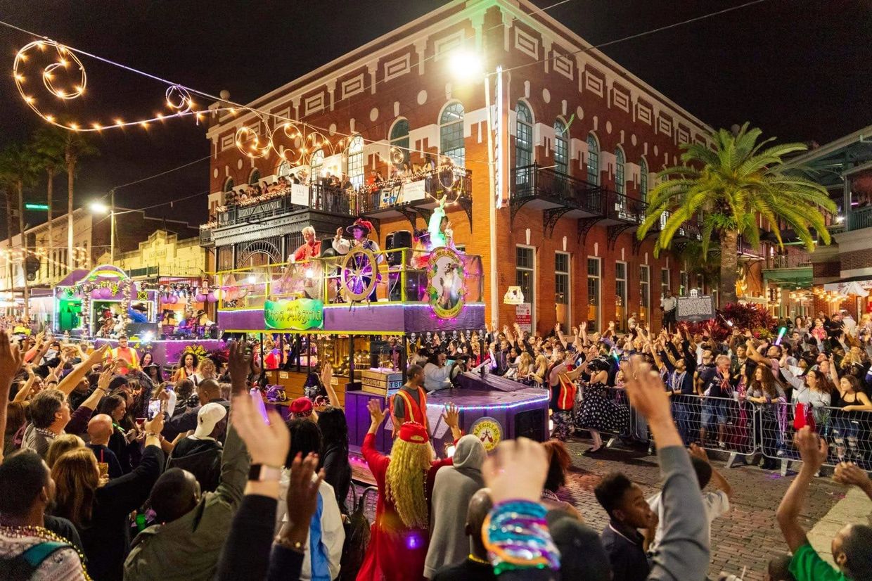 Crowds cheer along a colorful, lit parade float at night in a festive street celebration.