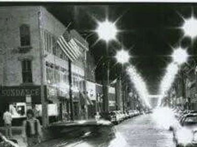 Black and white photo of a busy city street with vintage cars at night.