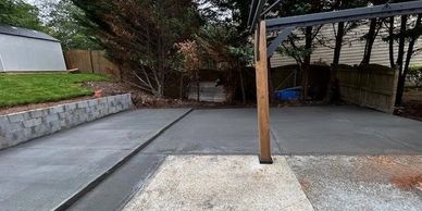 Freshly poured concrete driveway with a wooden post and stone retaining wall.