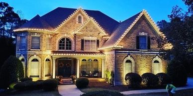 A large brick house decorated with warm white string lights at dusk.