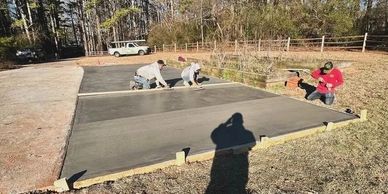 Three workers smoothing a freshly poured concrete slab outdoors.