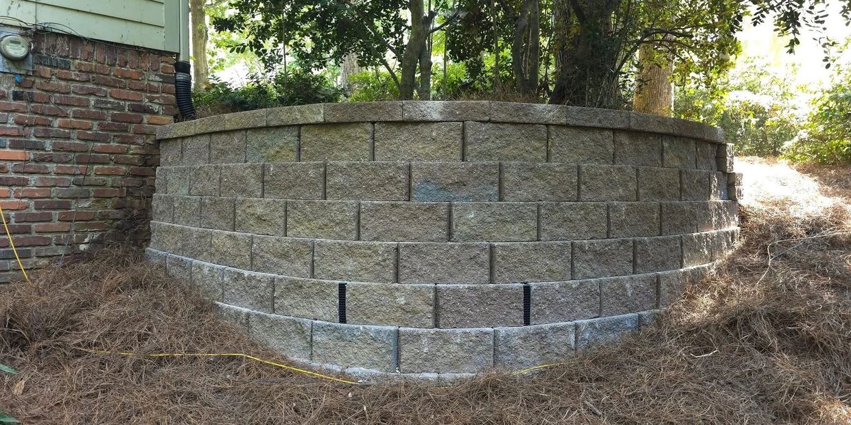 Curved retaining wall made of stone blocks surrounding a garden area.