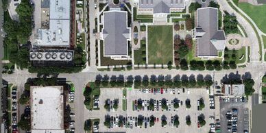 Aerial view of buildings, a parking lot, and green spaces with trees.