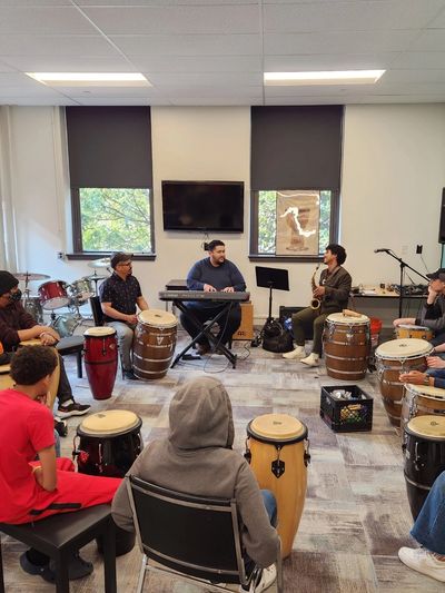 Group of people playing drums and keyboard indoors.