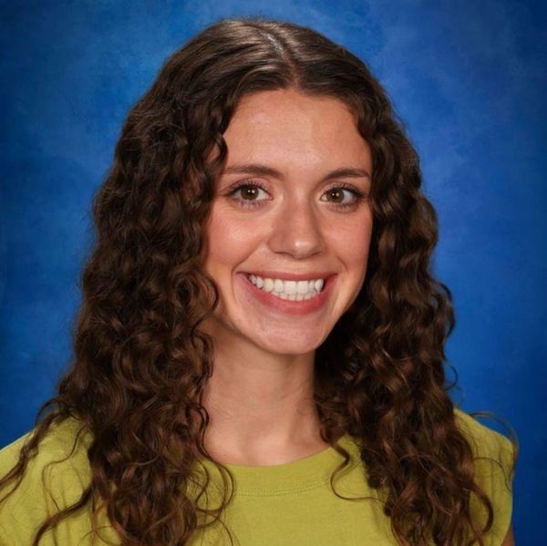 Young woman with curly hair smiling against a blue backdrop.