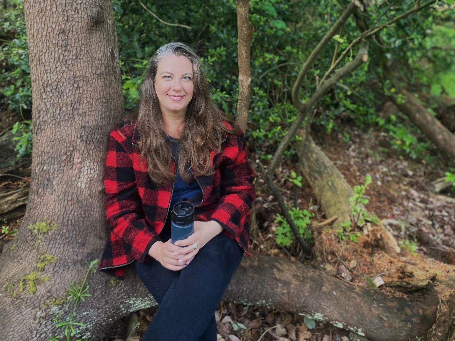 Life Coach, Laura, sits on large tree roots in the forest in Victoria BC