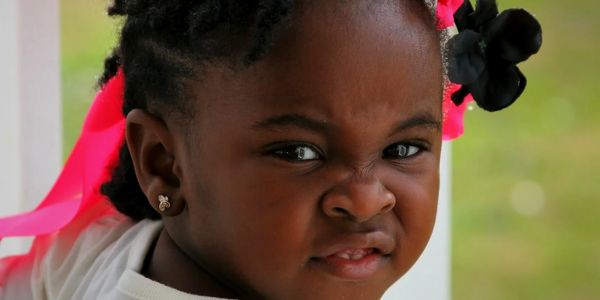 A young girl with a floral headband makes a scrunched face outdoors.