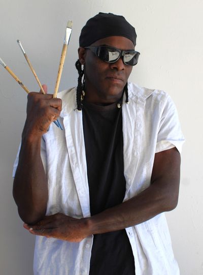 Artist posing confidently with paintbrushes in hand and sunglasses.