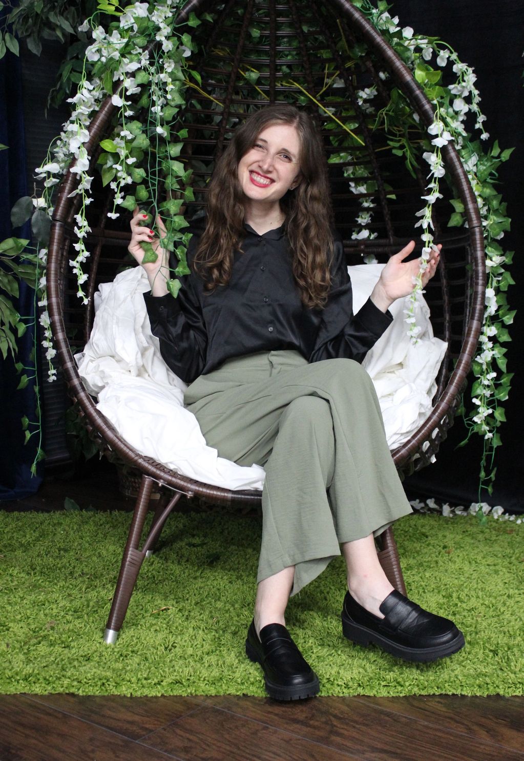 Young woman sitting on a hanging chair decorated with white flowers and green leaves.