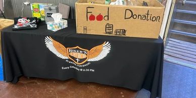 Food donation box sitting on a table with a Pikes Peak Bikers Church table cover.