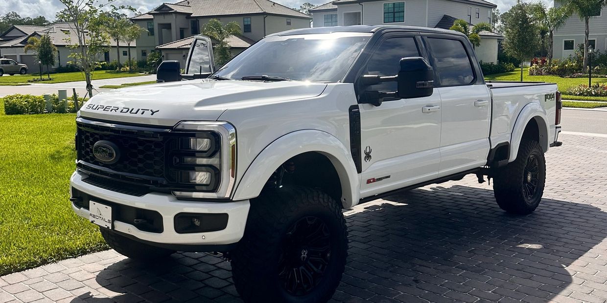 White Ford Super Duty truck parked on a driveway in a suburban neighborhood.