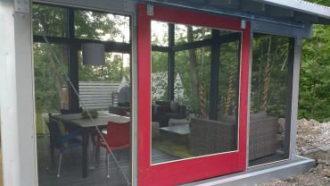 Modern glass patio enclosure with red sliding door and cozy interior.