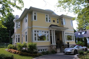 Elegant yellow two-story house with white accents and a sleek silver convertible parked outside.