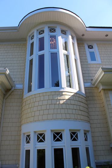 Curved bay window on a beige shingled house under a clear blue sky.
