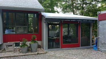 A small red and gray building with large windows and potted plants outside.