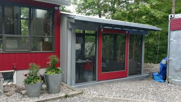 A red cabin with screened porch and potted plants outside.