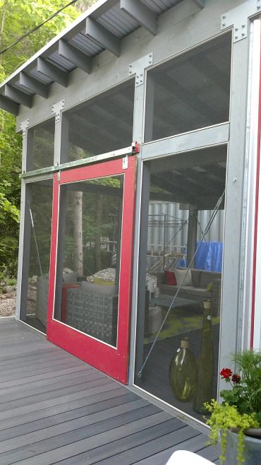 Modern screened porch with a red door and outdoor seating area.