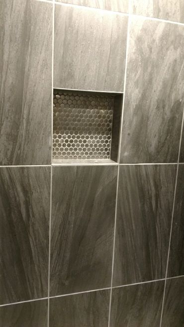 Gray tiled wall with a recessed niche featuring round mosaic tiles.