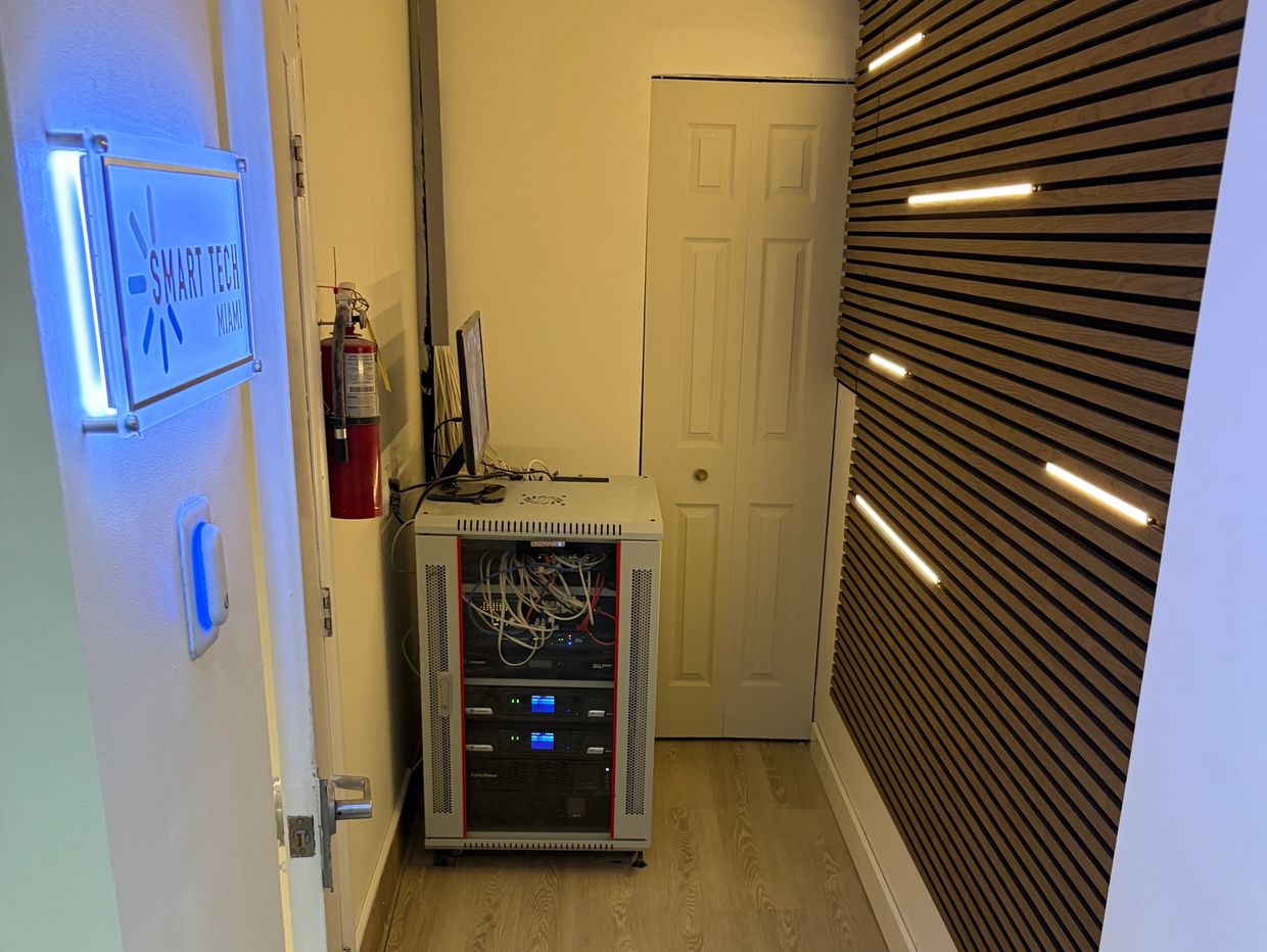 Tech room with server rack, blue neon sign, and modern wooden wall lights.
