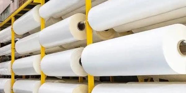 Large rolls of white fabric on yellow racks.
