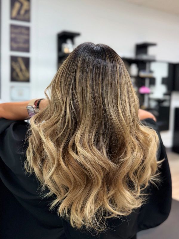 Long wavy blonde hair with dark roots styled in soft curls.