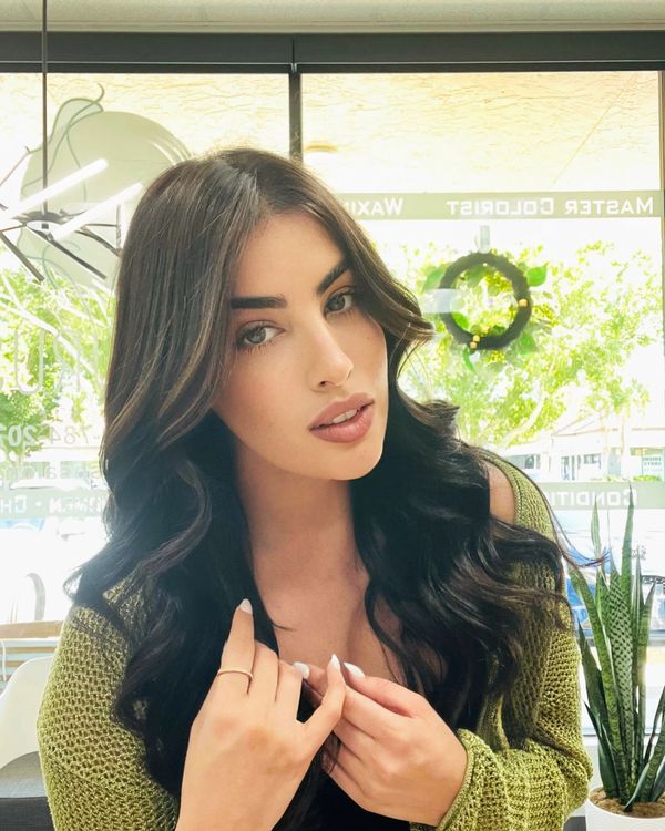 Young woman with long dark hair and green sweater looking at the camera indoors.