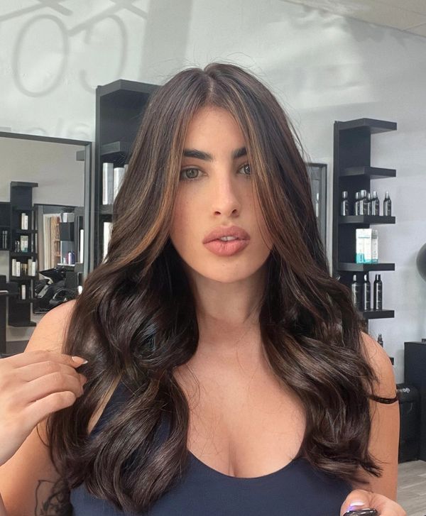 Woman with long, wavy dark hair and subtle highlights in a salon.